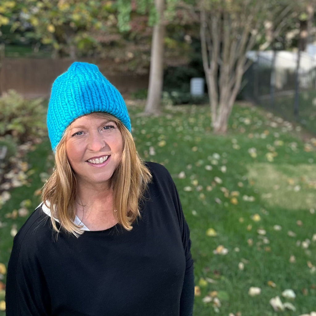 Woman standing in backyard wearing blue "Hey Boo Beanie" hat