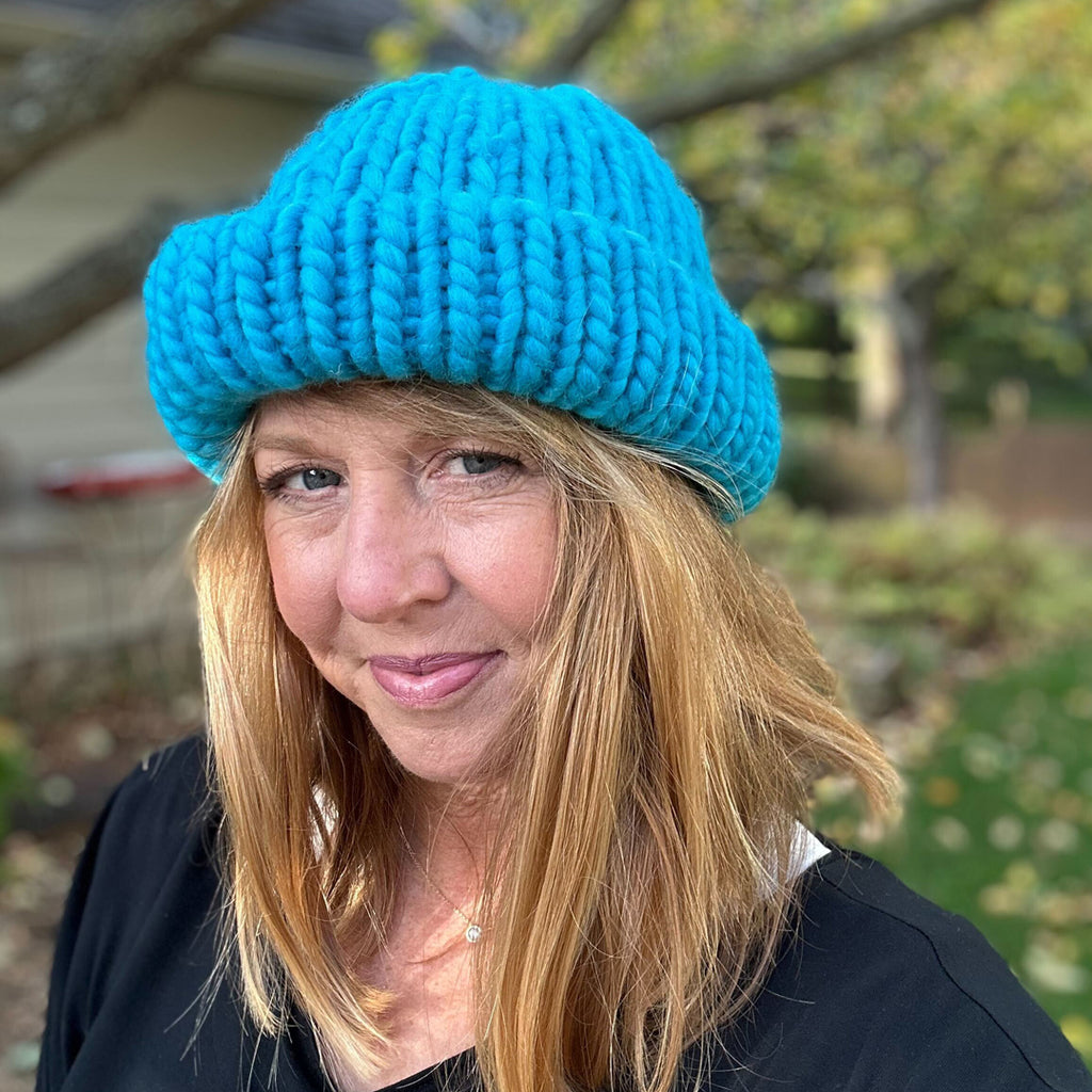 Woman standing in backyard wearing blue "Hey Boo Beanie" hat with brim folded up.