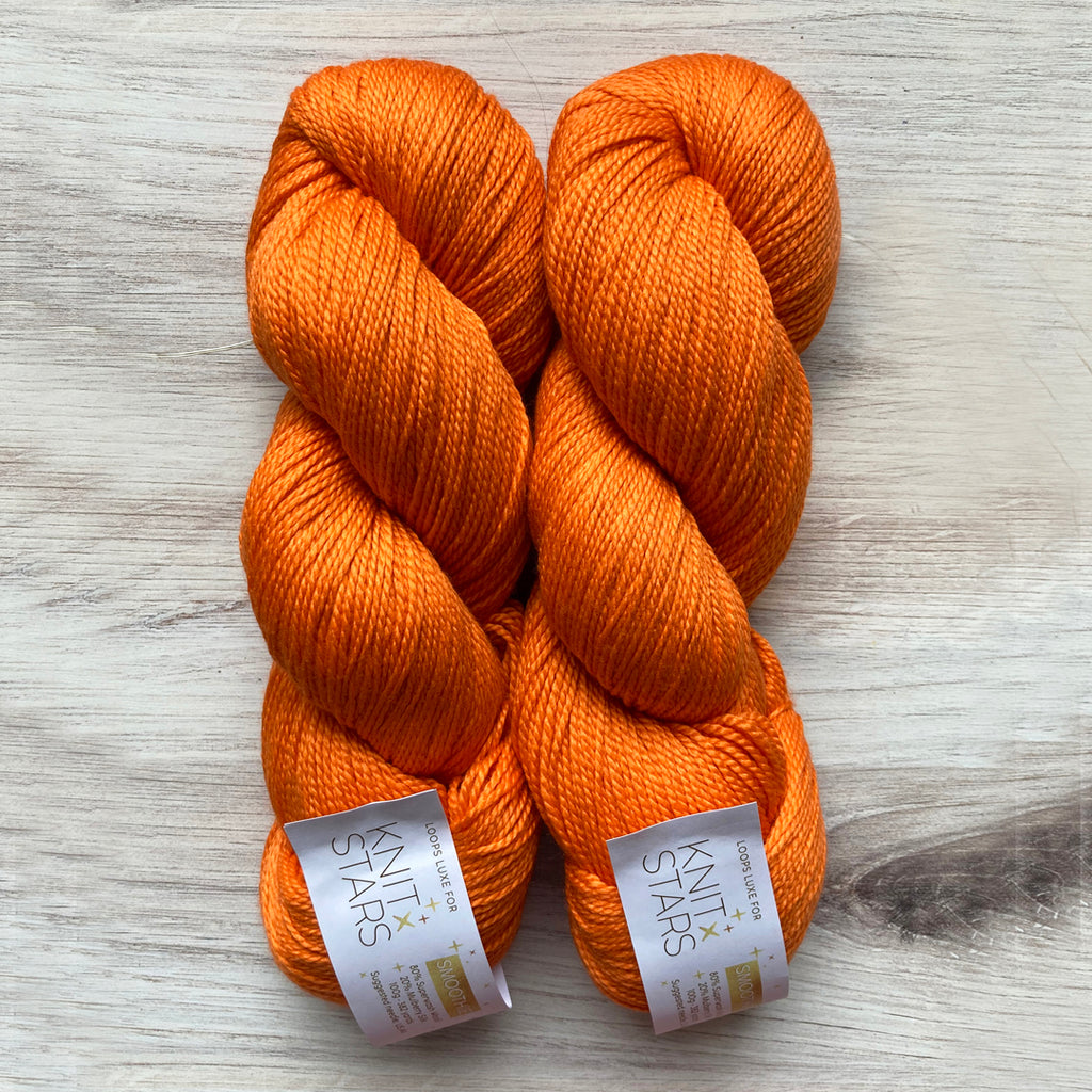 Two skeins of Loops Luxe Smoothie on table in colorway Iconic Orange